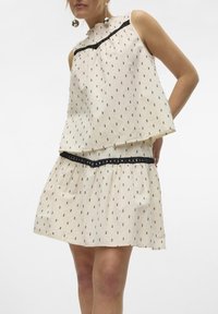 Light beige dress with short sleeves, featuring a gathered waist, black accents, and small black patterns throughout. Soft fabric texture.