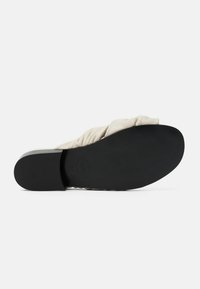 Sandalo scivoloso in tessuto beige caratterizzato da un design arricciato, una suola in gomma nera liscia e un tacco basso e squadrato.