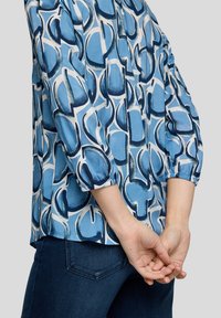 Blaue Bluse mit Muster, die ein geometrisches Design in Marineblau und Weiß zeigt, mit langen Ärmeln und elastischen Bündchen sowie einem lässigen Schnitt.