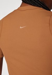 Close-up of a person wearing a ribbed, short-sleeve, light brown Nike shirt with a Nike swoosh logo centered on the upper back.