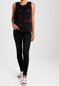 Svart ärmlös blus med blommönster, gathered halsringning; kombinerad med svarta smala jeans och silverfärgade slid sandals.