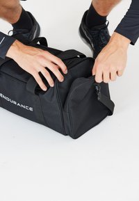 Musta urheilukassi, jossa on kaksi vetoketjullista osastoa, tukevat kahvat ja teksturoitu kangas. Brändinimi "ENDURANCE" painettuna valkoisella.