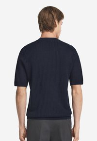 Mörkblå ribbad kortärmad tröja med rundad halsringning och strukturerad mönster. Lättviktig tyg, figurnära vid midjan och avslappnade ärmar.