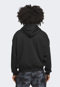 Sort hættetrøje med en stor hætte, sænkede skuldre og ribbede manchetter. Blød stoftekstur med en afslappet pasform. Bagfra ses et minimalistisk design.