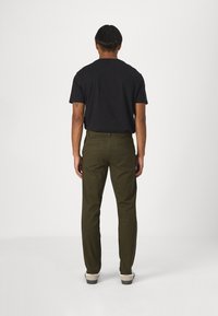 Svart kortärmad t-shirt kombinerad med olivgröna skräddarsydda byxor, med rak passform och bakfickor. Vita skor fulländar looken.