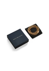 Zlati verižni zapestnica na črni usnjeni torbici, ob njej mornarsko modra kvadratna škatla z napisom "DANIEL WELLINGTON" v zlatem tisku.
