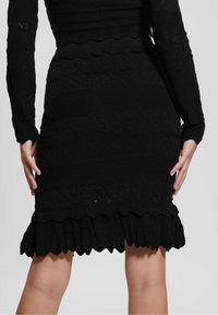 Robe noire en tricot à manches longues, présentant des motifs diagonaux et en vagues texturés, avec un ourlet volanté.