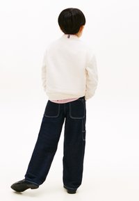 Λευκή φόρμα με ριγέ γιακά, συνδυασμένη με σκούρο τζιν, παντελόνι φαρδιά με τσέπες και αντίθετη ραφή. Μαύρα παπούτσια.