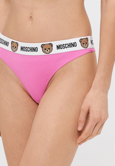 Roza bombažna tangica z belim pasom, ki vsebuje natisnjene risbe medvedov in besedilo "MOSCHINO". Brezšivne robove in nizko rez.