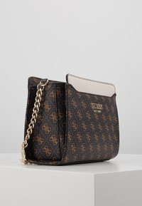 Hnědá kabelka se vzorem a zlatými akcenty, s řetízkovým popruhem a hladkým krémovým horním panelem. Disponuje logem na přední straně a má strukturovaný tvar.