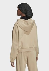 Felpa beige con cappuccio, dal taglio relax, con polsini a coste e tasche, abbinata a pantaloni beige coordinati. Un foulard nero texture completa l'outfit.
