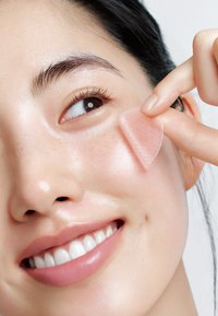 Un patch en gel translucide et clair est appliqué sur la peau sous l'œil, mettant en valeur une peau lisse, hydratée avec une légère brillance et une texture minimale.