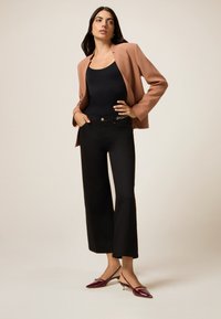 Top negro sin mangas, blazer marrón claro, jeans de pierna ancha negros de cintura alta y zapatos de tacón de charol burdeos con punta afilada.