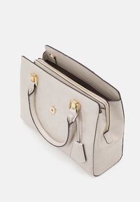 Cream textured handbag with double handles, gold-tone hardware, zippered central compartment, and attached keychain tag.