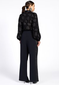 Black blouse with patterned texture and puffed sleeves paired with high-waisted, wide-leg trousers featuring satin side stripes.