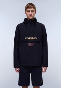 Marineblå vindjakke med lynlås i halsen, frontlomme og beige "NAPAPIJRI"-logo. Har et rødt og hvidt patch med det norske flagg på lommen.