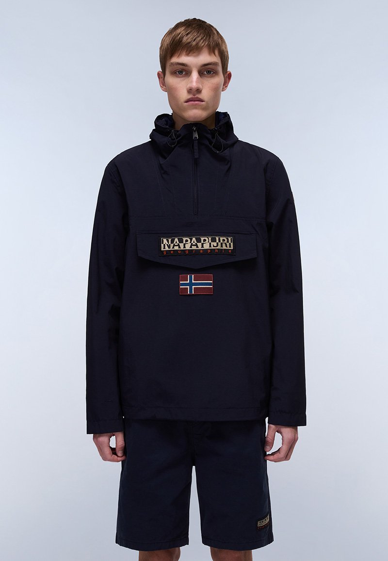 Marineblå vindjakke med lynlås i halsen, frontlomme og beige "NAPAPIJRI"-logo. Har et rødt og hvidt patch med det norske flagg på lommen.