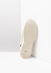 Semelle de sneaker beige avec un motif de grip texturé, dotée d'une semelle intermédiaire blanche et de détails du fabricant embossés sur le côté. Fabriqué en Italie.