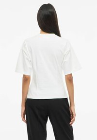 Biały T-shirt z krótkim rękawem, z okrągłym dekoltem i luźnym fasonem. Gładki bawełniany materiał, minimalistyczny design, brak widocznych wzorów lub akcentów.