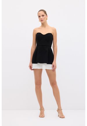 Vestido negro sin mangas con un cuerpo ajustado y una falda blanca plisada. El vestido presenta un escote corazón y una silueta acampanada.