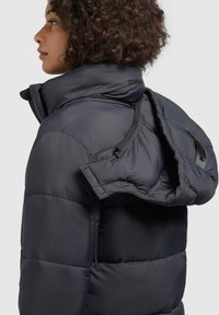 Navy puffer jacket featuring a stand collar, visible stitching, and a detachable hood. Material appears textured with a smooth finish.