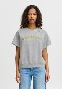 Pelēks džemperis ar īsām raglāna piedurknēm, ribinātu maliņu un zeltītu "TRÈS CHIC" tekstu krūšu rajonā. Mīksts kokvilnas maisījuma materiāls.