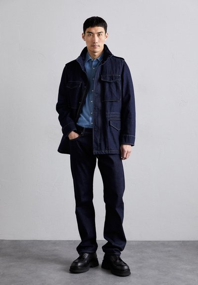 Dark blue denim jacket with four pockets, paired with a light blue shirt and dark blue jeans. Finished with black chunky shoes.