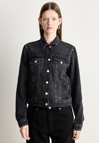 Mustat farkku takki, jossa on hopeiset niitit hartioilla, nappikiinnitys ja kaksi rintataskua. Ominaisuuksiin kuuluu klassinen kaulus ja lyhyt leikkaus.