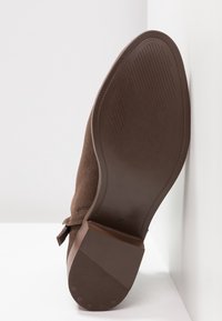 Hnědá semišová podrážka boty obrácená dopředu s texturovanými gripovými vzory a velikostí 37 vyraženou poblíž klenby.