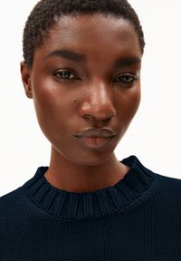 Marineblauer Strickpullover mit einem strukturierten, gerippten Halsausschnitt. Nahaufnahme, die Gesichtszüge, Hautfarbe und natürliche Lippenfarbe hervorhebt.