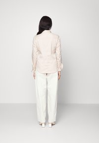 Ljusbeige button-up skjorta med puffärmar och sammanhållna detaljer, tillsammans med vita byxor med vida ben och klackade skor.