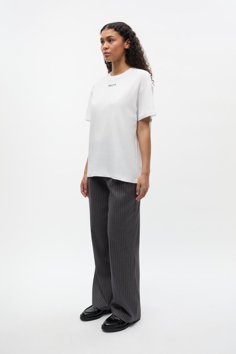Fehér rövid ujjú pamut póló "MELTY" felirattal. Szürke vékony csíkos, széles szárú nadrággal és fekete cipővel párosítva.