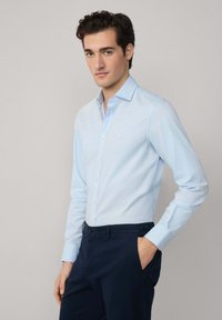 Lichtblauwe overhemden met lange mouwen, getailleerd ontwerp, lichte textuur; gecombineerd met donkerblauwe broeken, zichtbare zakken.