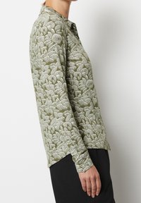 Camicia a maniche lunghe di colore verde oliva con texture a motivo foglia, polsini bottonati e colletto. Vestibilità casual, design con orlo piatto.