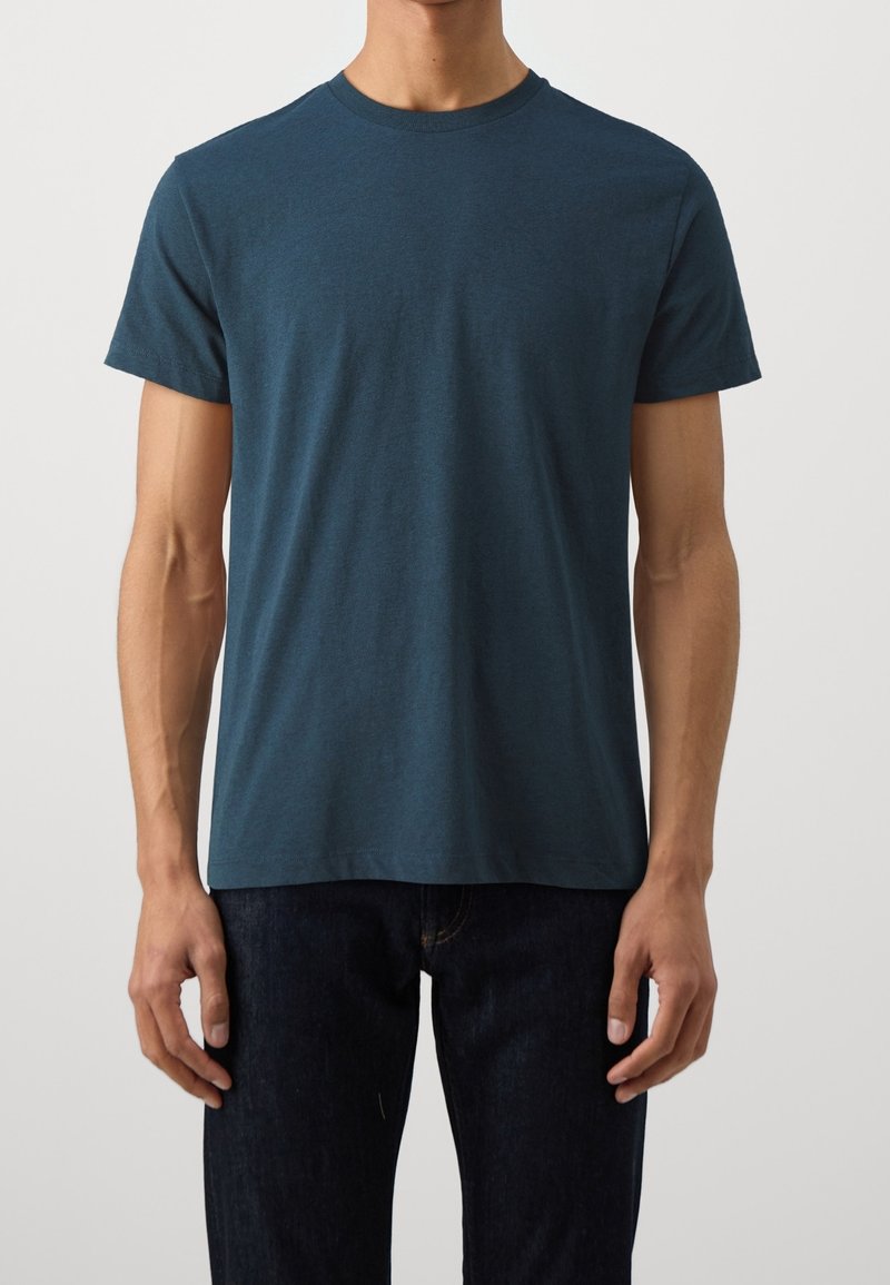 T-shirt à manches courtes en bleu sarcelle, fabriqué à partir d'un tissu doux, avec un col rond et une coupe décontractée, associé à un jean foncé.