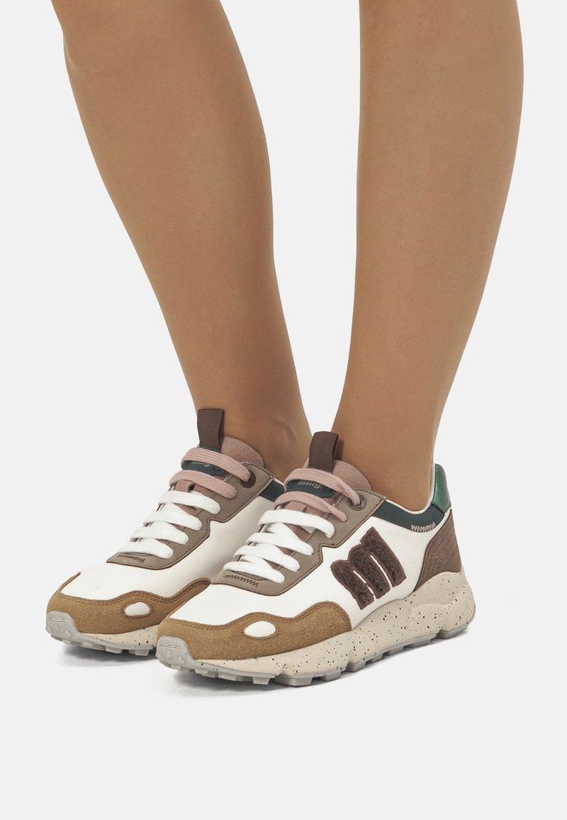 Sneakers con una tomaia in pelle bianca e marrone, caratterizzati da lacci rosa, accenti verdi e una suola beige maculata. Dettagli testurizzati notevoli sul lato.