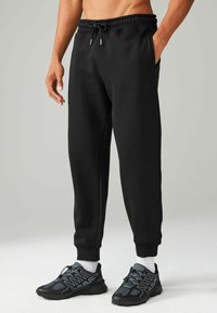 Pantalones deportivos negros hechos de tela suave, con una cinturilla elástica y cordón, bolsillos laterales y puños acanalados en los tobillos.