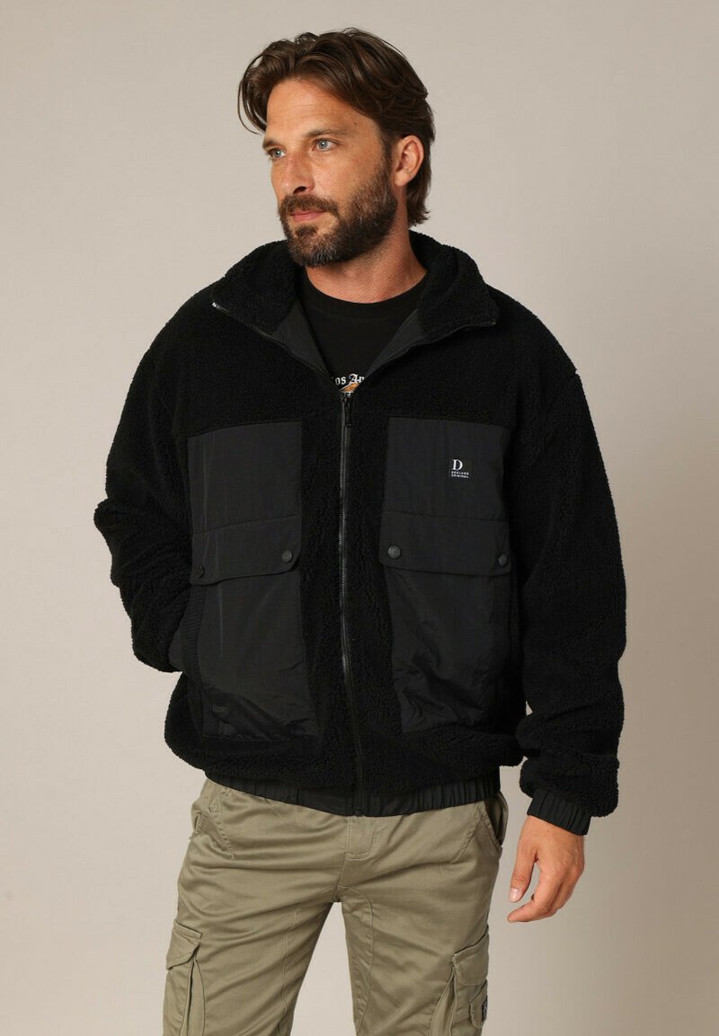 Zwarte fleecejas met contrasterende stoffen voorzakken. Ritssluiting aan de voorzijde, ribgebreide boorden en boord. Zachte, gestructureerde oppervlakte.