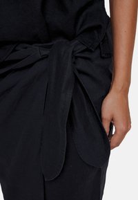 Sort tekstil i svart lin med knyttet livrem, glatt tekstur og flytende design. Stoffet ser lett og pustende ut.