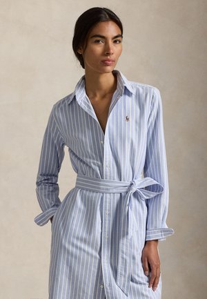 Φόρεμα πουκάμισο σε ανοιχτό μπλε και λευκές ρίγες με κουμπιά μπροστά, μακριά μανίκια και δέσιμο στη μέση, κατασκευασμένο από απαλό βαμβακερό ύφασμα. Φέρει ένα μικρό λογότυπο.
