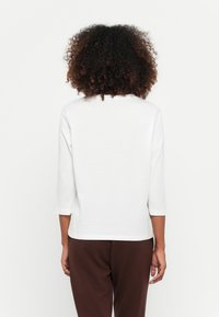 Witte top met driekwartmouwen, gemaakt van zachte stof, met een ronde halslijn en een relaxed fit, gecombineerd met bruine broek.