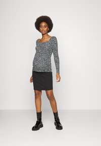 Top de manga longa impresso em preto e branco com decote quadrado, combinado com uma saia mini em preto canelada e botas de tornozelo brilhantes pretas.