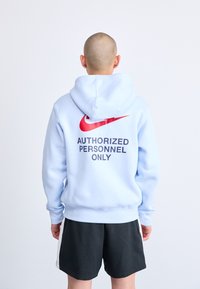 Sudadera azul claro de forro polar, con un gran logo de Nike en rojo y el texto negro "PERSONAL AUTORIZADO SOLAMENTE" en la parte posterior.