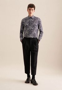 Langarmshirt in donkerblauw met een fijn wit bloemmotief; gecombineerd met zwarte geplooide broek en zwarte schoenen.