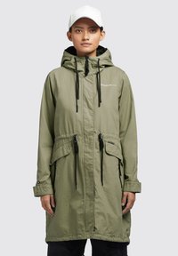 Parka de culoare verde măsliniu cu glugă, prevăzut cu șnururi ajustabile, buzunare laterale și un material ușor. Are un fermoar frontal și închideri cu capse.
