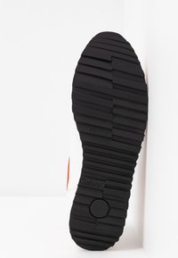 Semelle de chaussure en caoutchouc noir avec des rainures et des crêtes texturées ; présente un emblème circulaire et la marque "Gabor" sur le côté.