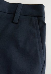 Pantalons navy en tissu lisse, dotés d'une ceinture, de poches latérales et de coutures soignées. La texture semble robuste et bien finie.