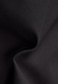 Zbliżenie czarnego tkanego materiału z widocznym wzorem splotu, przedstawiające fałdy i cienie podkreślające jego grubość i strukturę.