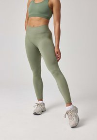 Set di abbigliamento attivo verde composto da un reggiseno sportivo senza cuciture e leggings a vita alta, realizzati in un tessuto morbido e elastico con una superficie liscia e un design aderente.