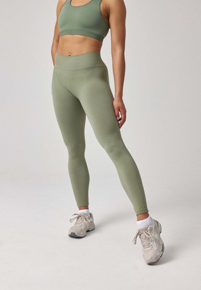 Set di abbigliamento attivo verde composto da un reggiseno sportivo senza cuciture e leggings a vita alta, realizzati in un tessuto morbido e elastico con una superficie liscia e un design aderente.